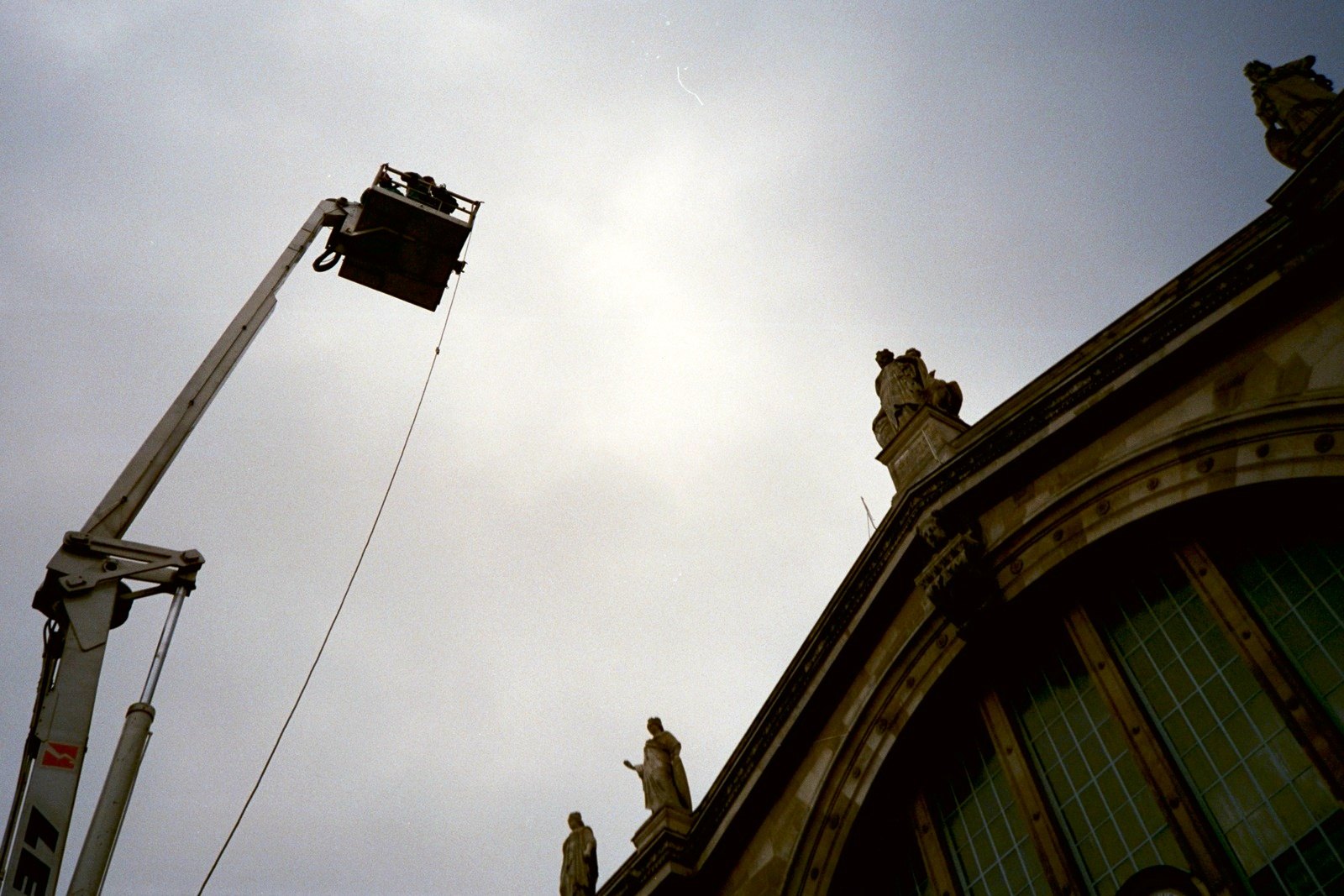 A crane arm holding a film lamp against a grey sky, beside the arched facade of the Gare du Nord