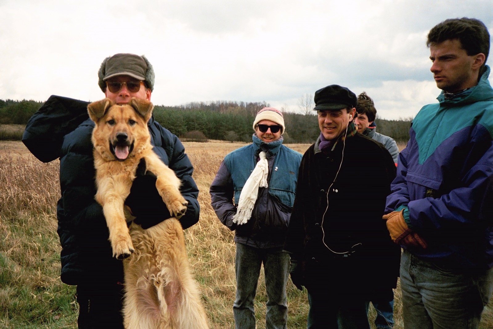 Five people in winter coats in a field, one of them holding up a large golden dog